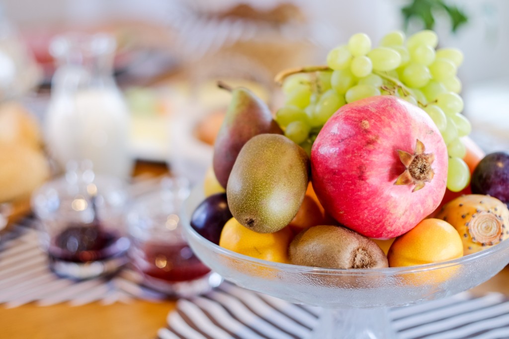 A glass bowl of fruit: grapes, a pomegranate, pears, and kiwi.