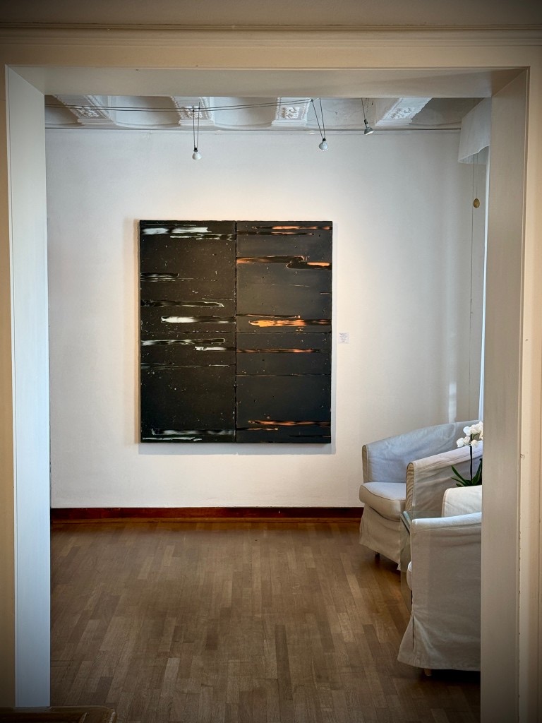 A dark painting seen through a doorway, with pale armchairs beside it.