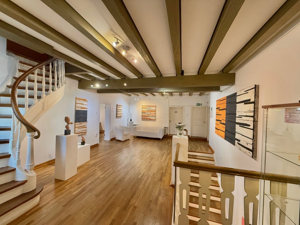 The gallery rooms, with a wooden floor, paintings, sculpture and a staircase.