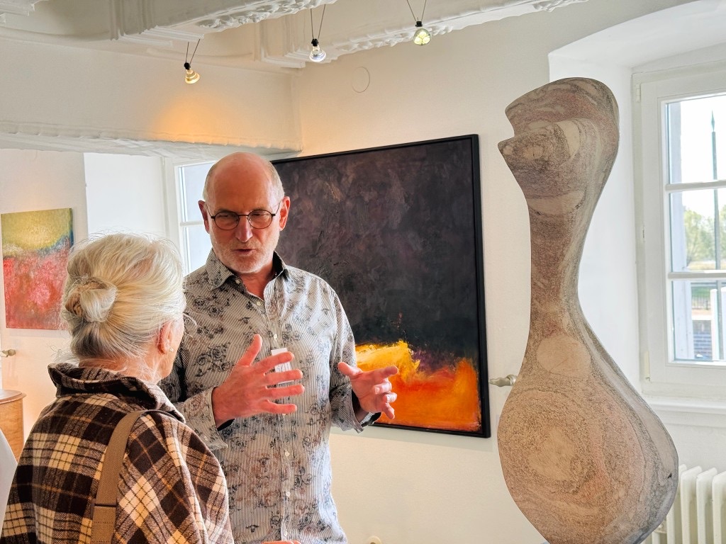 A conversation beside a sculpture and a painting in the gallery.