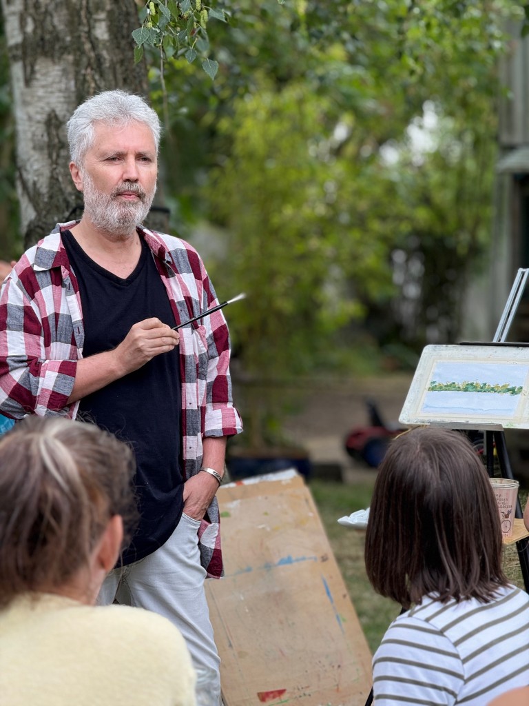A man with a brush, painting outdoors with others.