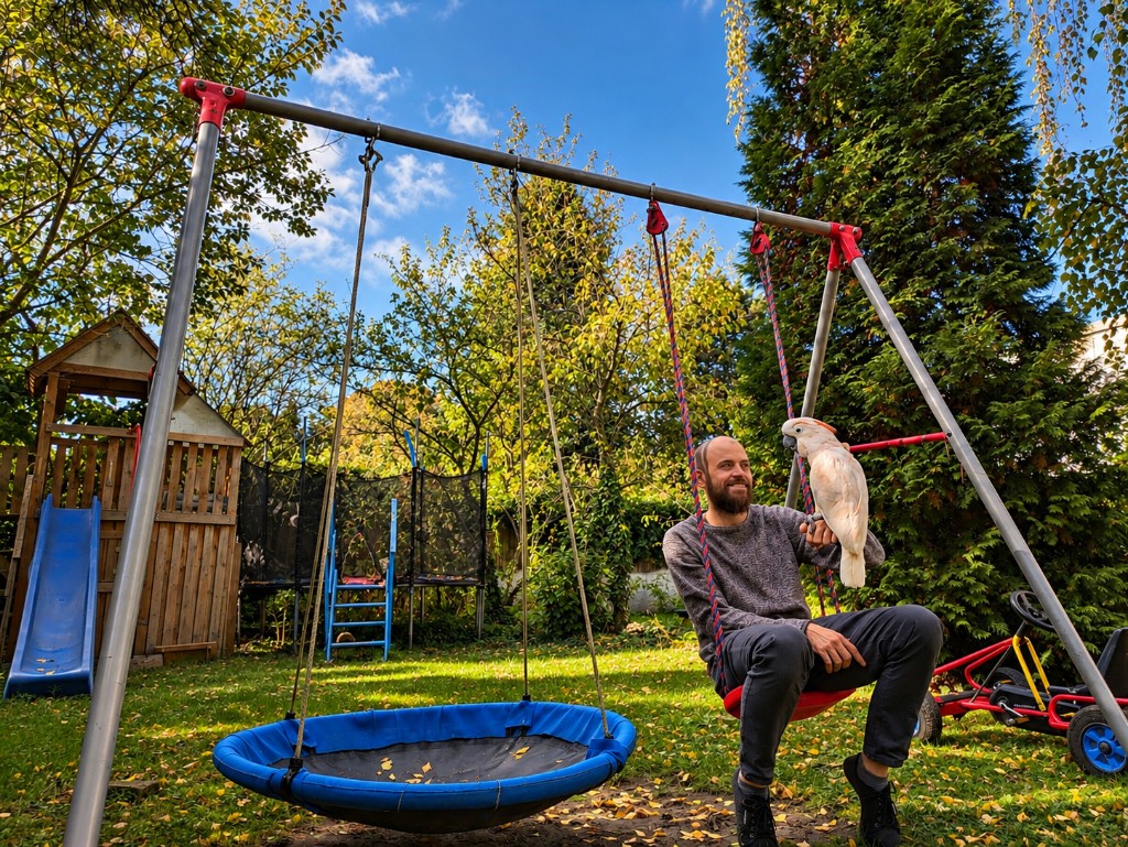 A man with a cockatoo on a swing in the garden.