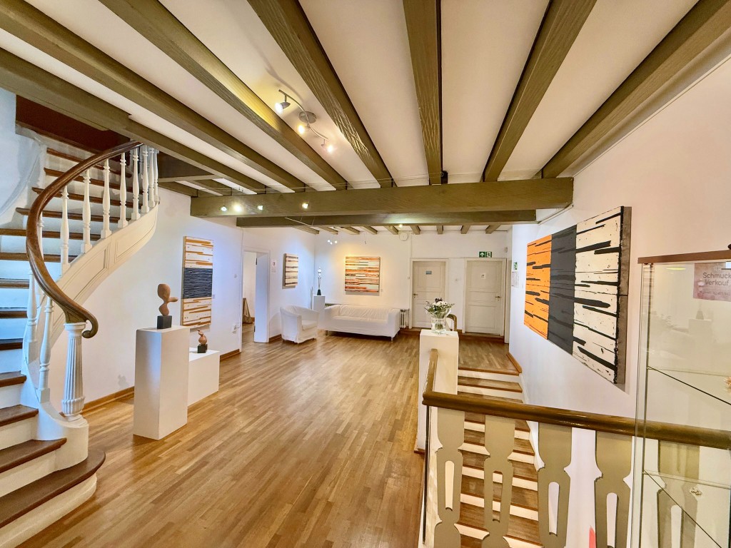 A gallery room with paintings, a staircase, and wooden beams.