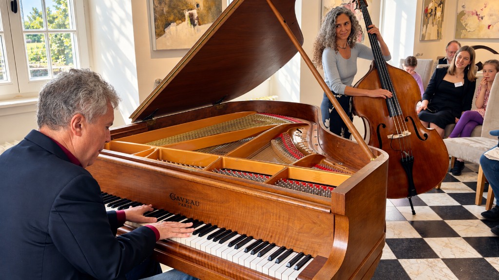 A grand piano and a double bass in the hall, with people listening.