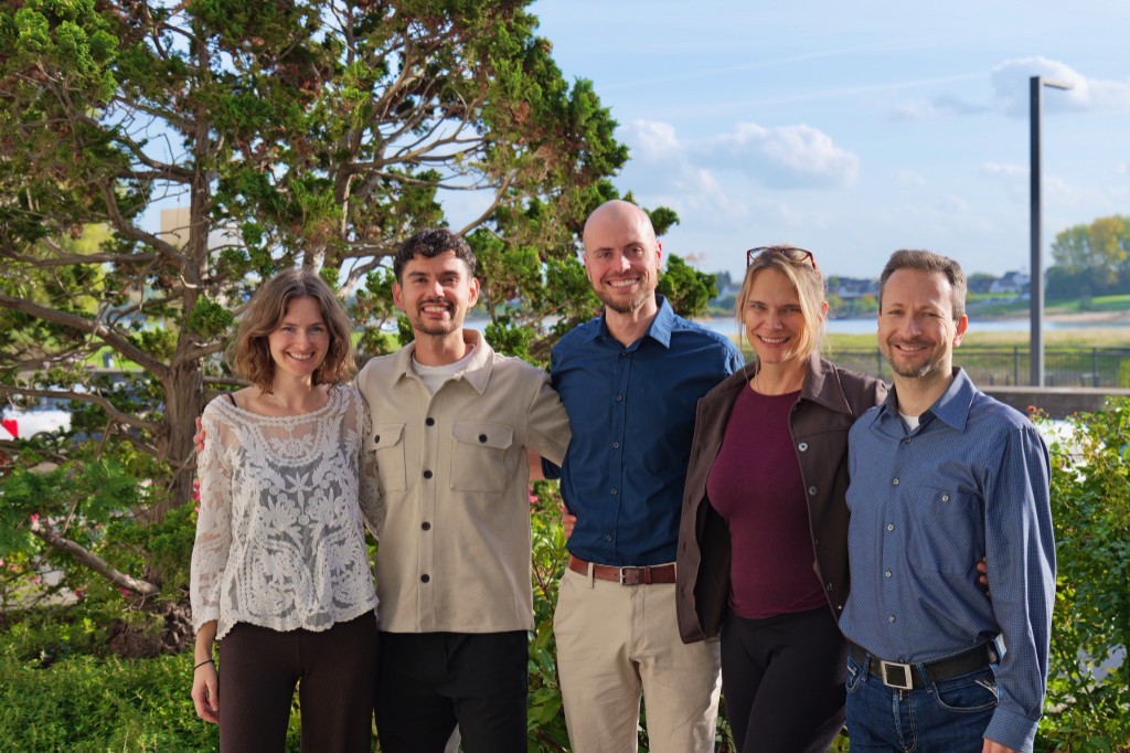 Five people standing together outdoors by the water.