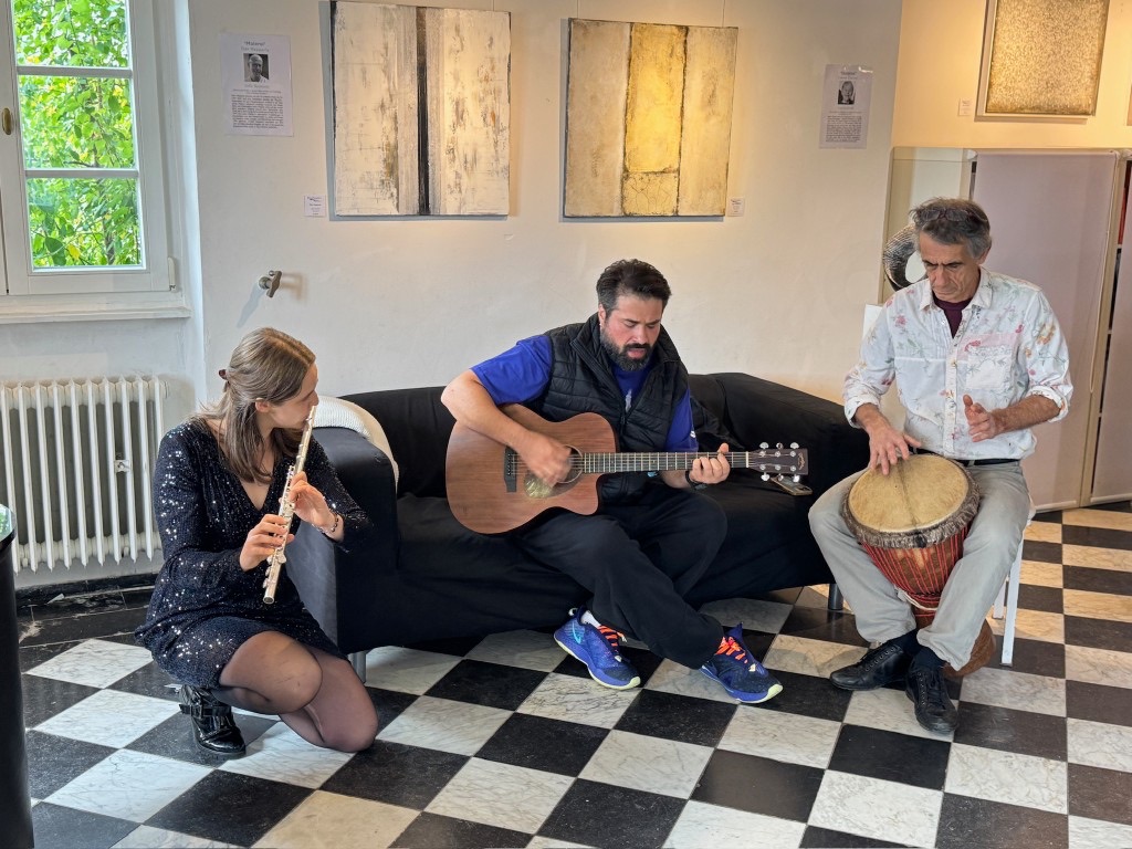 Three musicians with flute, guitar and drum in the hall, paintings on the wall.