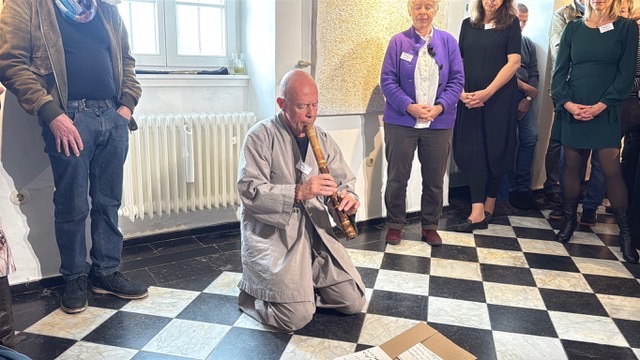 A musician with a wind instrument on the chequered floor of the hall.