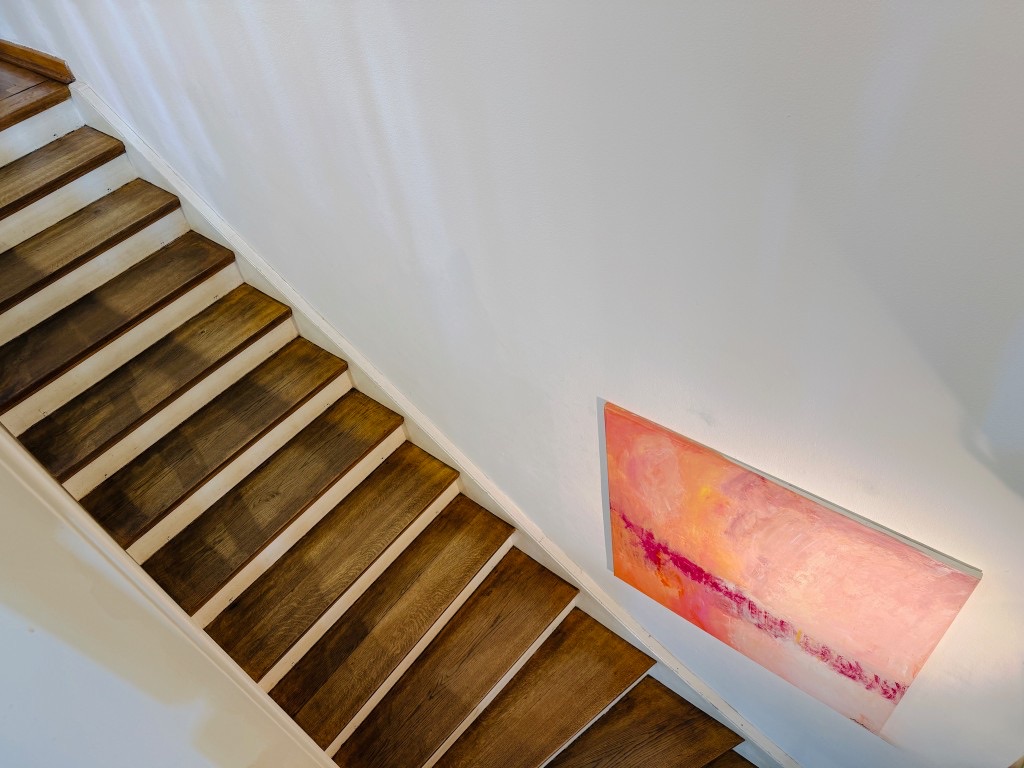 Wooden stairs beside a painting on a white wall.