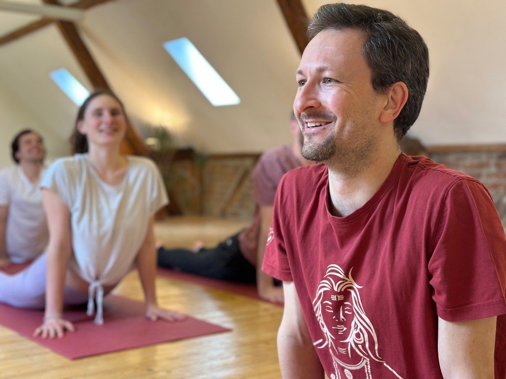 Übung im Haus, mit Raum zum Lachen. Ein Gast lächelt neben einer Yoga-Haltung im Yoga Hotel zwischen Köln und Düsseldorf.